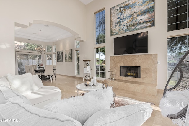 living room featuring an inviting chandelier, a fireplace, a high ceiling, and a tray ceiling