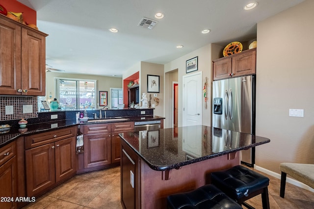 kitchen with dark stone counters, a kitchen breakfast bar, sink, a kitchen island, and stainless steel appliances