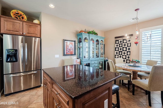 kitchen with a center island, a notable chandelier, dark stone countertops, stainless steel fridge, and light tile patterned floors