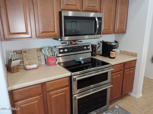 kitchen featuring brown cabinets, light tile patterned floors, appliances with stainless steel finishes, and light countertops