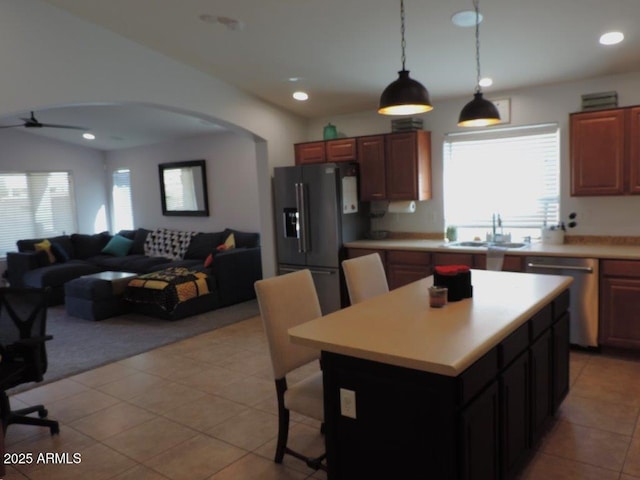 kitchen with arched walkways, stainless steel appliances, a sink, open floor plan, and light countertops