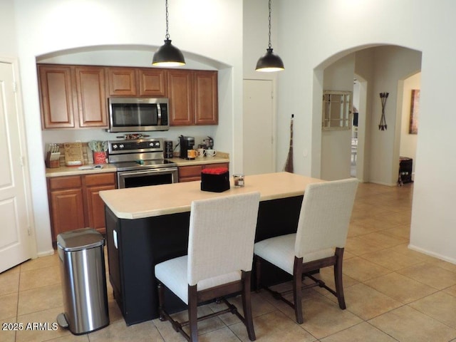 kitchen featuring arched walkways, brown cabinets, decorative light fixtures, stainless steel appliances, and light countertops