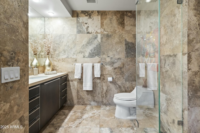 bathroom featuring walk in shower, vanity, toilet, tile walls, and visible vents