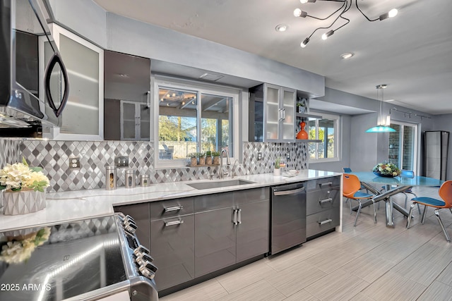 kitchen with tasteful backsplash, sink, hanging light fixtures, light stone countertops, and stainless steel appliances