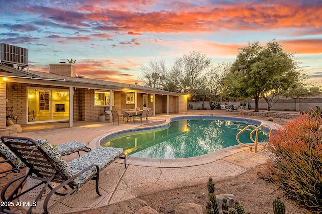 pool at dusk with central air condition unit and a patio area