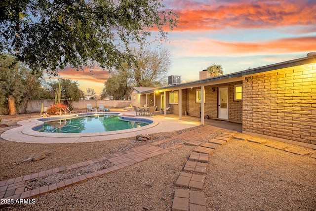 pool at dusk featuring central AC unit and a patio