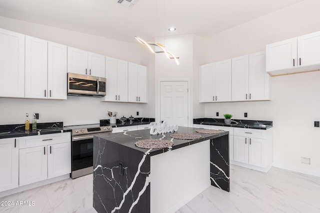 kitchen featuring marble finish floor, appliances with stainless steel finishes, white cabinets, a kitchen island, and dark stone counters