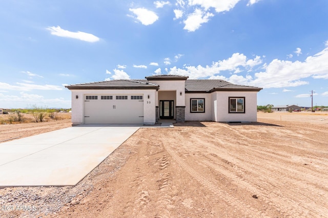 prairie-style home featuring a garage, driveway, a tile roof, and stucco siding