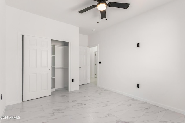 unfurnished bedroom featuring a closet, marble finish floor, baseboards, and a ceiling fan