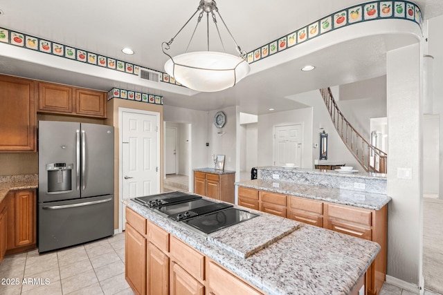 kitchen with stainless steel refrigerator with ice dispenser, decorative light fixtures, a kitchen island, black electric stovetop, and light stone countertops