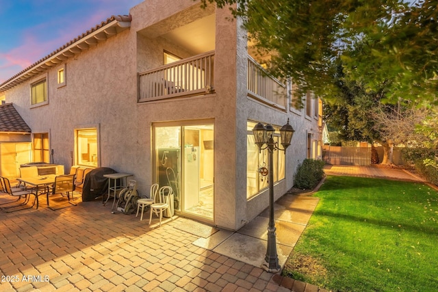 back house at dusk featuring a balcony, a yard, and a patio area