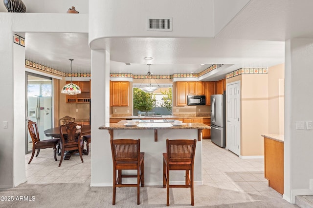 kitchen featuring pendant lighting, stainless steel fridge, a breakfast bar, and light stone counters