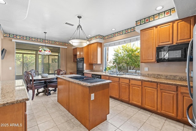 kitchen with sink, hanging light fixtures, black appliances, light stone countertops, and a kitchen island