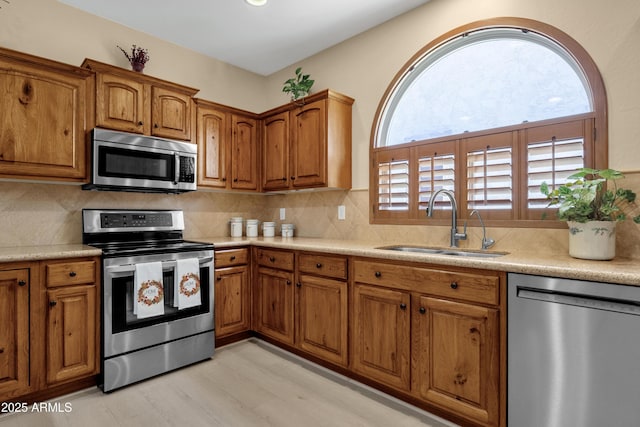 kitchen with light countertops, backsplash, appliances with stainless steel finishes, brown cabinetry, and a sink