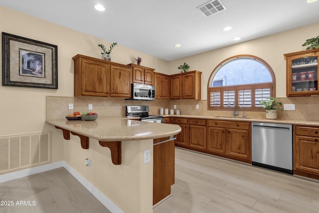 kitchen featuring appliances with stainless steel finishes, brown cabinetry, visible vents, and a sink