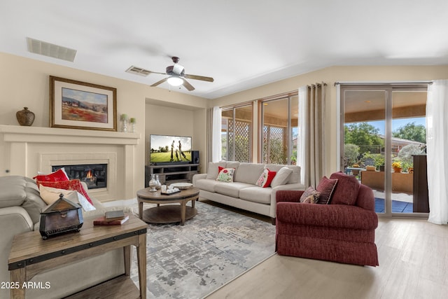 living room featuring ceiling fan, wood finished floors, a glass covered fireplace, and visible vents