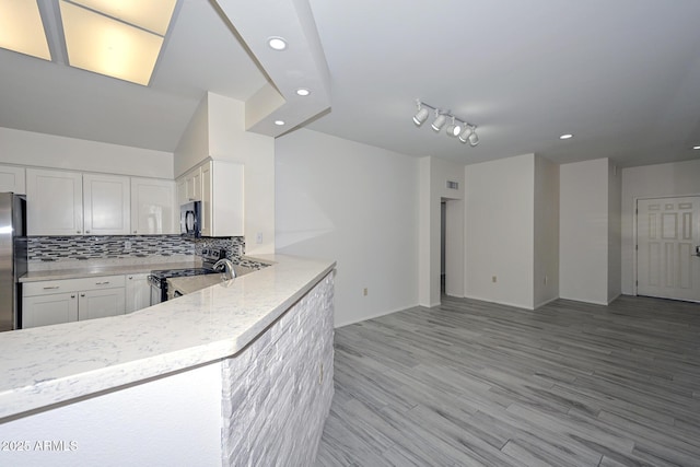 kitchen featuring backsplash, white cabinets, light hardwood / wood-style flooring, appliances with stainless steel finishes, and kitchen peninsula