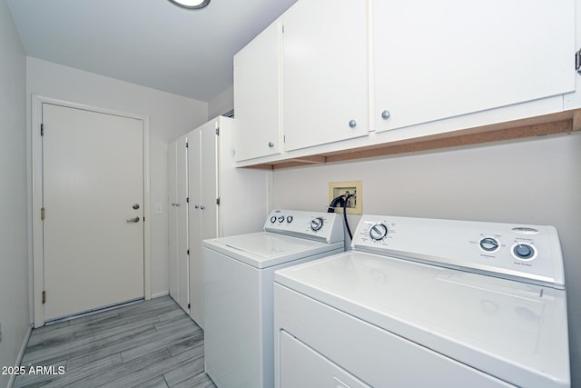 laundry area with washing machine and clothes dryer, light hardwood / wood-style flooring, and cabinets