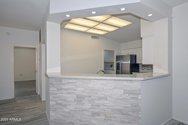 kitchen featuring kitchen peninsula, stainless steel fridge, backsplash, hardwood / wood-style floors, and white cabinetry