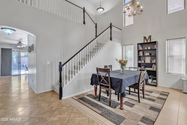 dining room featuring tile patterned floors, arched walkways, ceiling fan with notable chandelier, and baseboards