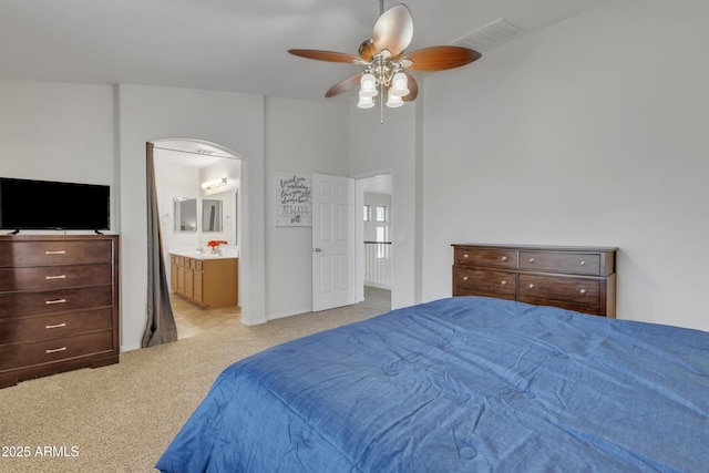 bedroom featuring visible vents, connected bathroom, a ceiling fan, light carpet, and arched walkways