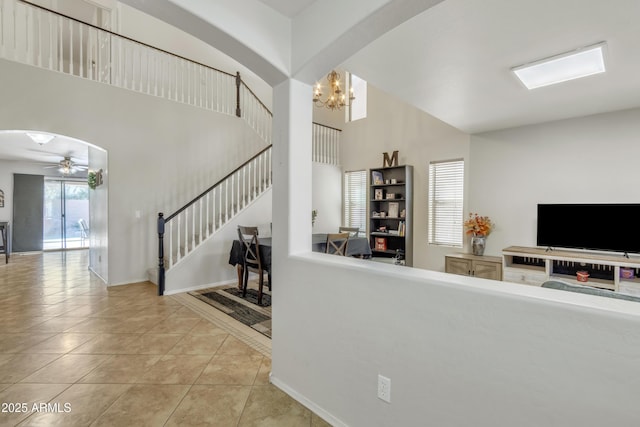 tiled living area with stairway, a high ceiling, baseboards, ceiling fan with notable chandelier, and arched walkways