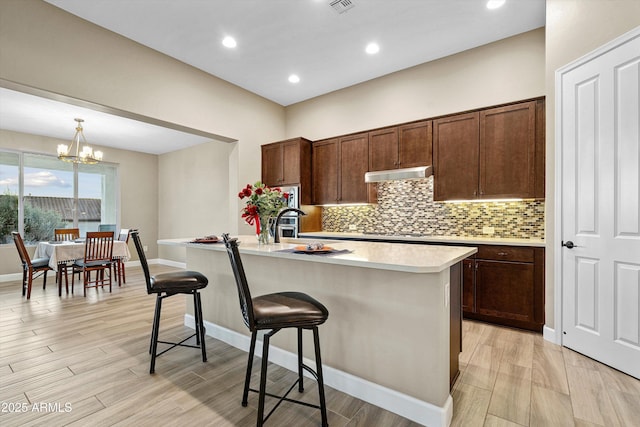 32128 S Bighorn Dr, Oracle, AZ 85623 - kitchen with under cabinet range hood, light countertops, tasteful backsplash, a kitchen bar, and a chandelier