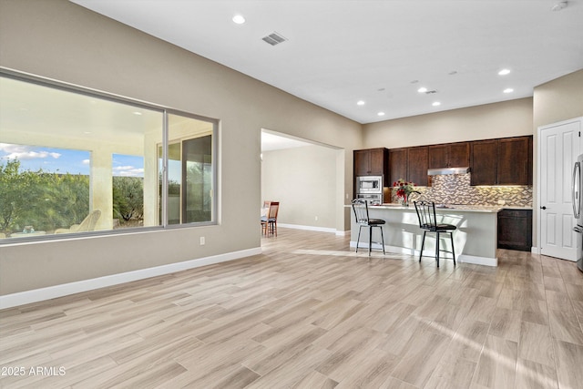 32128 S Bighorn Dr, Oracle, AZ 85623 - kitchen with under cabinet range hood, light countertops, tasteful backsplash, dark brown cabinets, and an island with sink