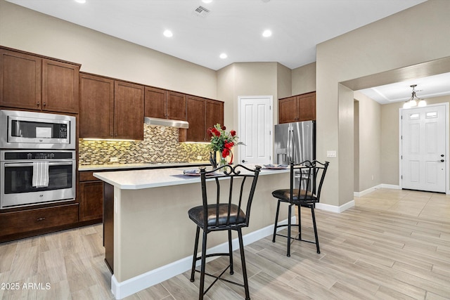 32128 S Bighorn Dr, Oracle, AZ 85623 - kitchen featuring appliances with stainless steel finishes, under cabinet range hood, a breakfast bar area, decorative backsplash, and light countertops