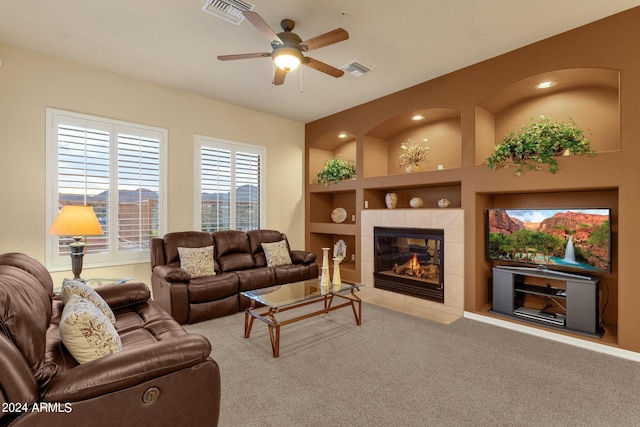 living room featuring built in shelves, ceiling fan, a tile fireplace, and carpet floors