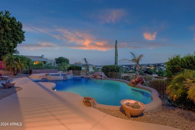 pool at dusk with a patio and an in ground hot tub