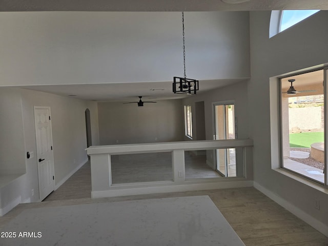 interior space with light wood-style flooring, baseboards, arched walkways, and a ceiling fan