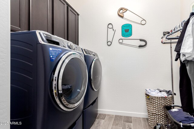 clothes washing area featuring cabinet space, baseboards, washer and clothes dryer, and light wood-style floors