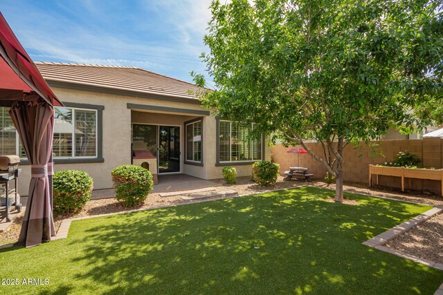 rear view of property featuring a yard, stucco siding, a tiled roof, and fence