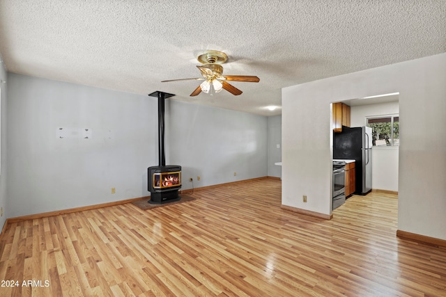 unfurnished living room with light hardwood / wood-style flooring, a textured ceiling, a wood stove, and ceiling fan