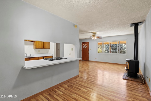 unfurnished living room with ceiling fan, a textured ceiling, light hardwood / wood-style floors, a wood stove, and sink