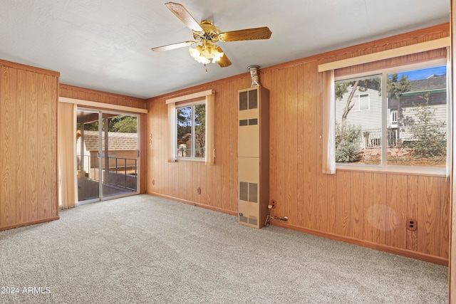 unfurnished room with ceiling fan, wooden walls, and light colored carpet