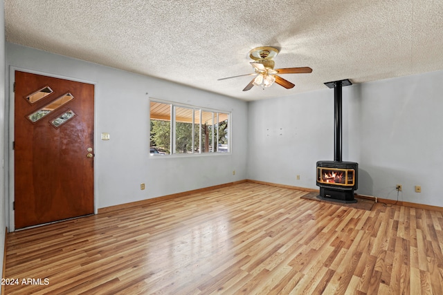 unfurnished living room with light hardwood / wood-style flooring, a wood stove, and a textured ceiling