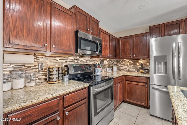 kitchen featuring appliances with stainless steel finishes, backsplash, light stone counters, a textured ceiling, and light tile patterned flooring