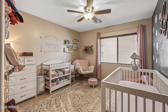 bedroom with light tile patterned floors, a crib, and ceiling fan