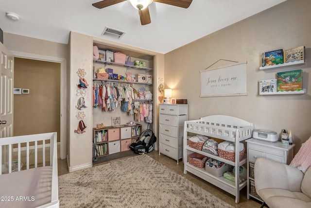 tiled bedroom featuring a nursery area, ceiling fan, and a closet