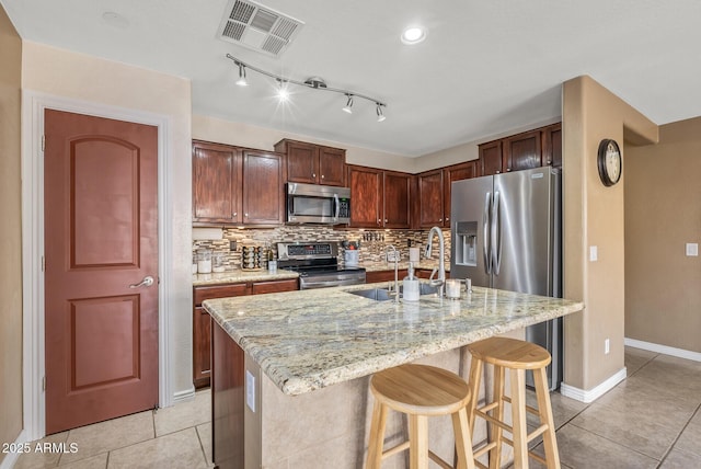 kitchen with stainless steel appliances, an island with sink, light stone countertops, and a kitchen breakfast bar