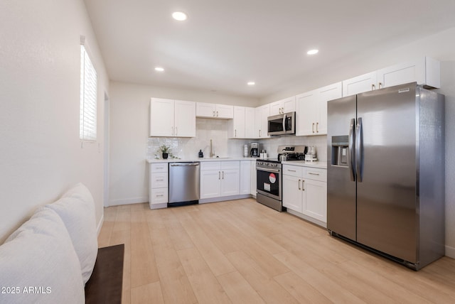 kitchen featuring stainless steel appliances, sink, white cabinetry, light hardwood / wood-style floors, and tasteful backsplash