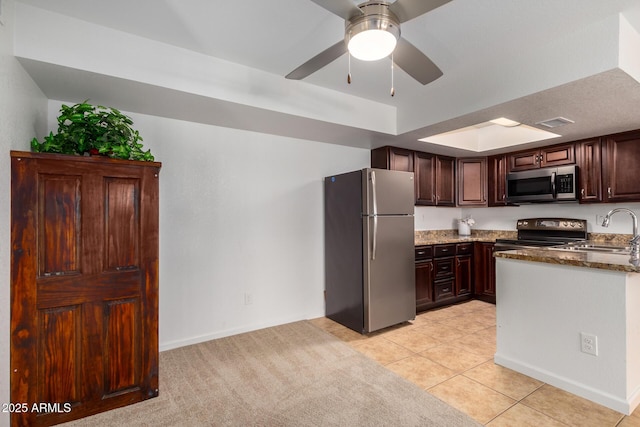 kitchen with a sink, dark brown cabinetry, stainless steel appliances, and dark stone countertops