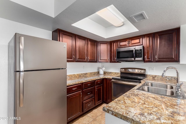 kitchen with visible vents, appliances with stainless steel finishes, a sink, light tile patterned floors, and a tray ceiling