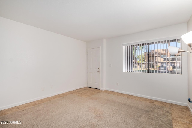 carpeted empty room featuring baseboards and tile patterned floors