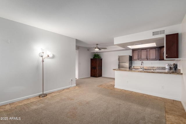 kitchen with visible vents, freestanding refrigerator, a peninsula, ceiling fan, and a sink