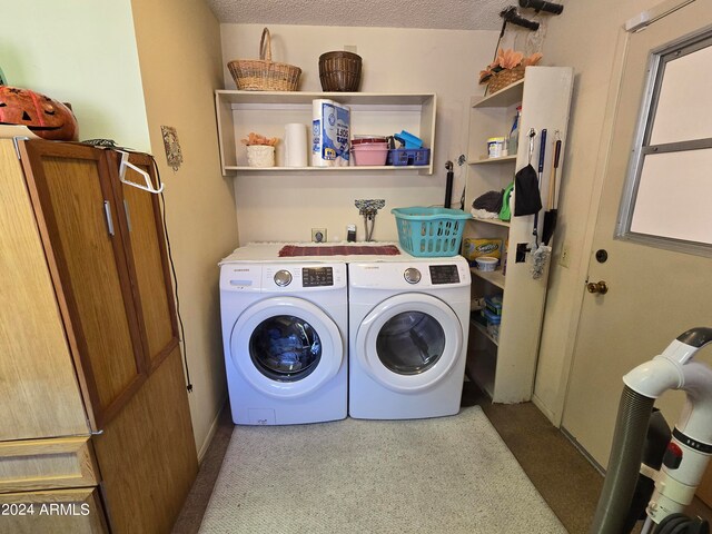 clothes washing area with washer and clothes dryer, light carpet, and a textured ceiling