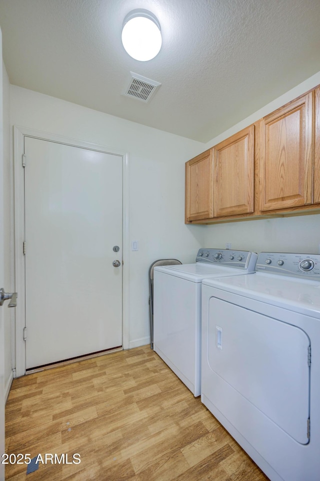 washroom featuring cabinets, a textured ceiling, washer and dryer, and light wood-type flooring