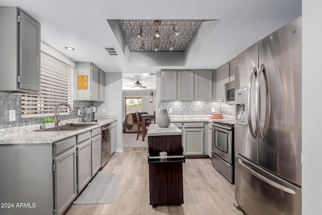 kitchen featuring appliances with stainless steel finishes, a raised ceiling, sink, a center island, and light hardwood / wood-style floors